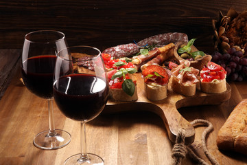 Traditional italian antipasto bruschetta appetizer with cherry tomatoes, cream cheese, basil leaves and balsamic vinegar on cutting board with prosciutto, salami, cheese