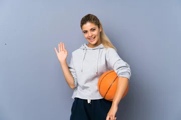 Foto op Aluminium Teenager girl playing basketball over grey wall saluting with hand with happy expression © luismolinero