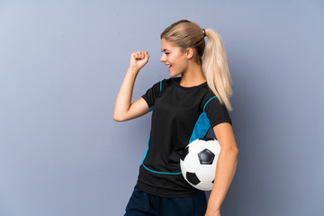 Blonde football player teenager girl over grey wall