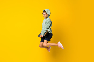 Blonde teenager skater girl jumping over isolated yellow background © luismolinero