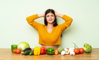 Fototapeta premium Teenager girl with many vegetables frustrated and takes hands on head