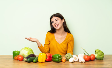 Fototapeta premium Teenager girl with many vegetables holding copyspace imaginary on the palm to insert an ad