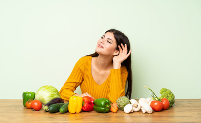 Teenager girl with many vegetables listening to something by putting hand on the ear