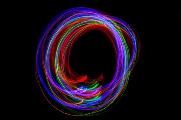Long exposure photograph of neon multi colour in an abstract swirl parallel lines pattern against a black background. Light painting photography.