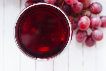glass of red wine and grapes on white wooden table