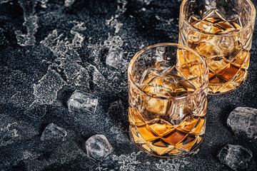 Whiskey with ice on stone dark background.