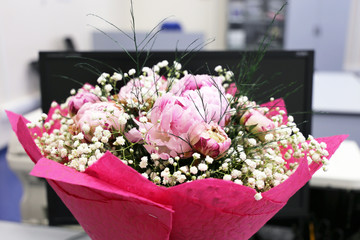 Bouquet of flowers on a table in front of a PC monitor. Birthday or wedding in a office, surprise for colleague at work, concept of celebration in a team