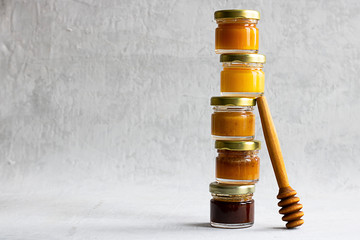 Five Small glass jar with metal cap with different kinds and colours of honey one on another and spoon isolate and on grey cement background with copy space. Healthy product, natural. Horizontal