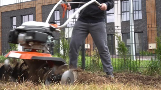Strong man working with petrol cultivator on plowing townhouse yard