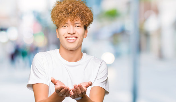 Young handsome man with afro hair wearing casual white t-shirt Smiling with hands palms together receiving or giving gesture. Hold and protection