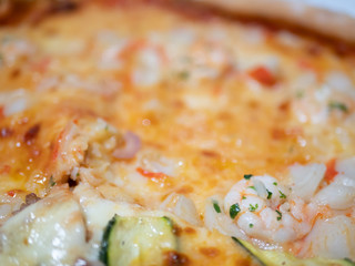 Close up of an Italian pizza with zucchini shrimp crabmeat, mozzarella and tomato.