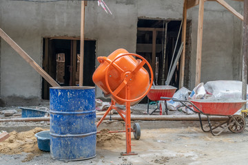 Orange concrete mixer prepares cement mortar. Concrete mixer, barrels against the background of a...