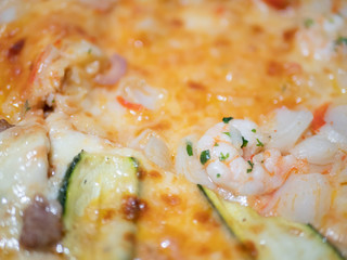 Close up of an Italian pizza with zucchini shrimp crabmeat, mozzarella and tomato.