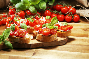 Traditional italian antipasto bruschetta appetizer with cherry tomatoes, cream cheese, basil leaves and balsamic vinegar on cutting board. Antipasti