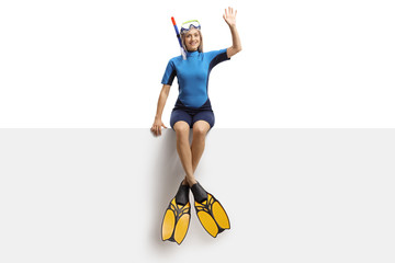 Young woman in a wetsuit, a diving mask and flippers sitting on a banner and waving