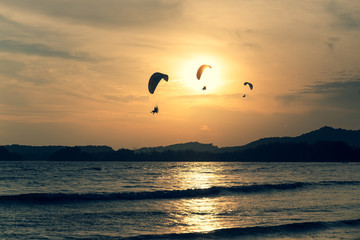 Beautiful Silhouette of paraglider flying in the sky of sunset on the beach.