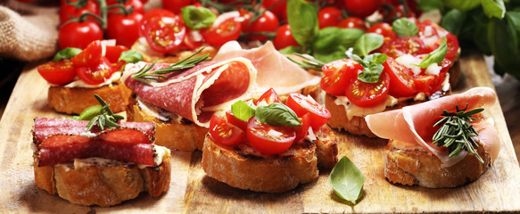 antipasto various appetizer. Cutting board with prosciutto, salami, cheese, bread and olives on dark wooden background