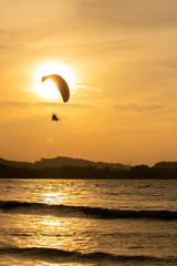 beautiful Silhouette of paraglider flying in the sky of sunset on the beach.