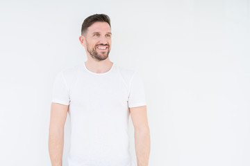 Young handsome man wearing casual white t-shirt over isolated background looking away to side with smile on face, natural expression. Laughing confident.