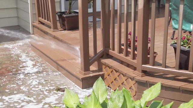 Slow motion view of pressure power washing of wooden deck and steps in a backyard with puddle of water with soap suds visible