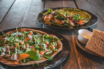 Delicious Italian vegetarian pizza with green leaves, spinach, carrots and radishes on a wooden background
