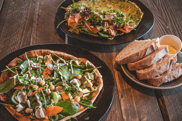 Delicious Italian vegetarian pizza with green leaves, spinach, carrots and radishes on a wooden background