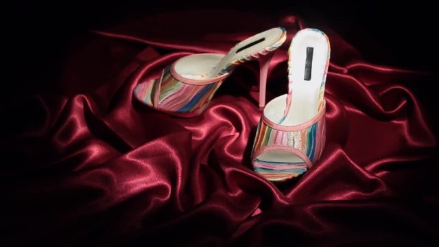 Approaching, pair of pink clogs with high heels standing on a red cloth.