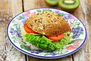 Mixed grain roll with cheese, lettuce and tomato on colorful vintage plate