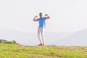 Well dressed ( fashionable) man stands in nature looking over a cliff at the large lake and mountain line while wearing boat shoes, polo shirt and formal pants.