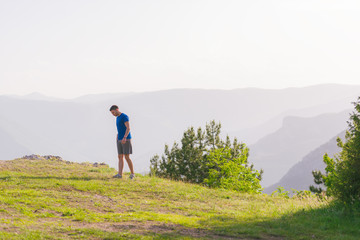 A fit male athlete is preparing for a work out in nature while looking over a cliff at the large lake and mountain line.