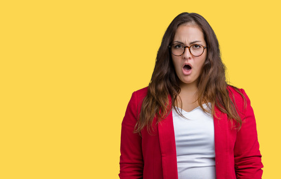 Beautiful plus size young business woman wearing elegant jacket and glasses over isolated background In shock face, looking skeptical and sarcastic, surprised with open mouth