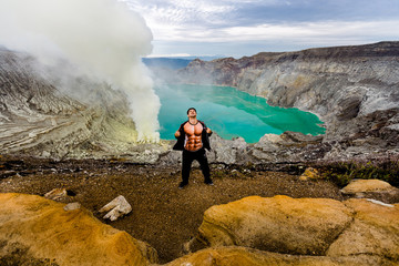 A young man is having fun around in the crater of a volcano against the background of a green...