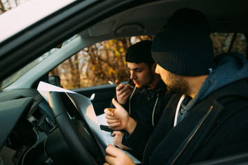 Two armed bandits sitting in a car planning their next robbery, while counting on a stopwatch the time they have for the robbery, showing off their guns and pointing at the blueprint.