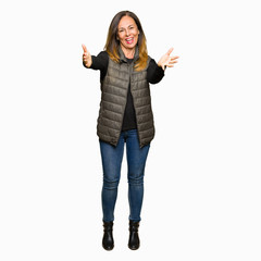 Obraz premium Beautiful middle age woman wearing winter vest looking at the camera smiling with open arms for hug. Cheerful expression embracing happiness.