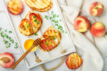 Gourmet summer Breakfast - sandwiches (bread toast, bruschetta) with grilled peaches, cream cheese (ricotta, mascarpone), thyme and honey on an old white wooden table. Selective focus
