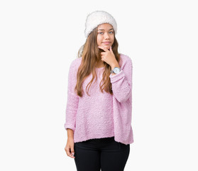 Young beautiful brunette woman wearing sweater and winter hat over isolated background looking...