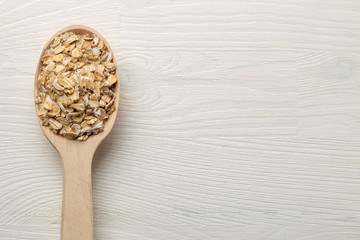 Dry oatmeal flakes in a wooden spoon on a white wooden table. healthy nutrition. healthy food. top view