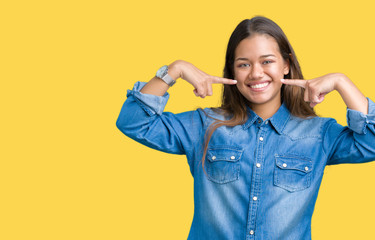 Young beautiful brunette woman wearing blue denim shirt over isolated background smiling confident showing and pointing with fingers teeth and mouth. Health concept.