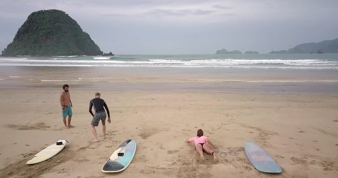 Aerial footage of people who are learning surfing. Surfer students. Handsome man teach young sportsmen how to paddle. Sporty summer camp. Water adventure vacation. Tropical hipster holiday. Bali surf.