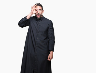 Young Christian priest over isolated background doing ok gesture shocked with surprised face, eye...