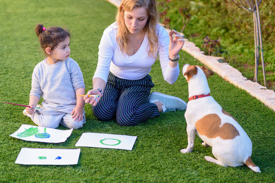 Happy family with Jack Russell Terrier dog drawing and playing in summer garden. Family love, summer vacation, holiday, learning concept.