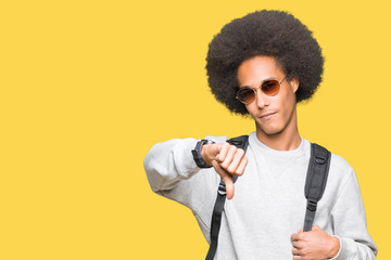 Young african american man with afro hair wearing sunglasses and backpack with angry face, negative...