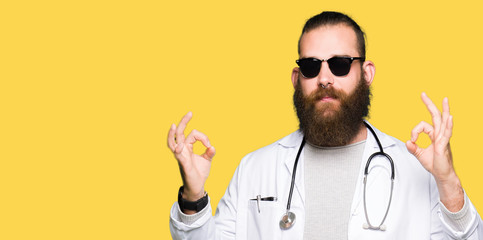 Young blond doctor man with beard wearing sunglasses relax and smiling with eyes closed doing meditation gesture with fingers. Yoga concept.