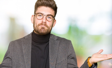 Young handsome business man wearing glasses clueless and confused expression with arms and hands...