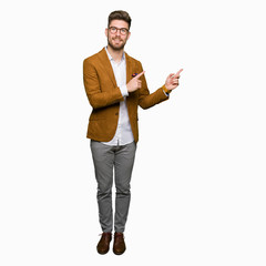 Young handsome business man wearing glasses smiling and looking at the camera pointing with two hands and fingers to the side.