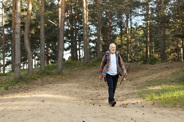 Naklejka premium Outdoor picture of sad elderly bearded man with fishing rod going along path in woods, having disappointed facial expression because he caught no fish at all. on fishing spot Activity and recreation