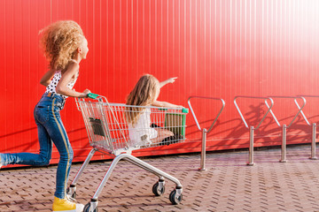 2 girls having fun and having fun with a grocery cart against the background of a red wall