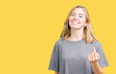Beautiful young woman wearing oversize casual t-shirt over isolated background Beckoning come here gesture with hand inviting happy and smiling