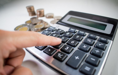 Women's hand is calculating coins with a calculator. Close up.