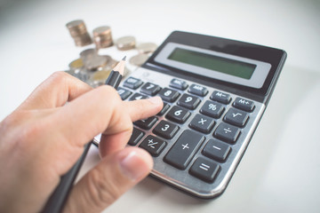 Man's hand hold a pencil and a calculator a lot of coins with a calculator. Close up.